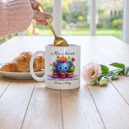 Personalised teacher thank you mug with cute watercolour cactus illustration in terracotta pots, personalised with 'Mrs Norris' and 'Thank You For Helping Me Grow From Amy' in script font, on a wooden table with a croissant and pink rose