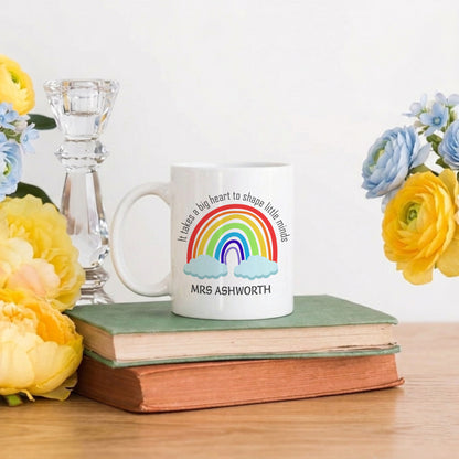 White mug with rainbow design and text on a stack of books with flowers around