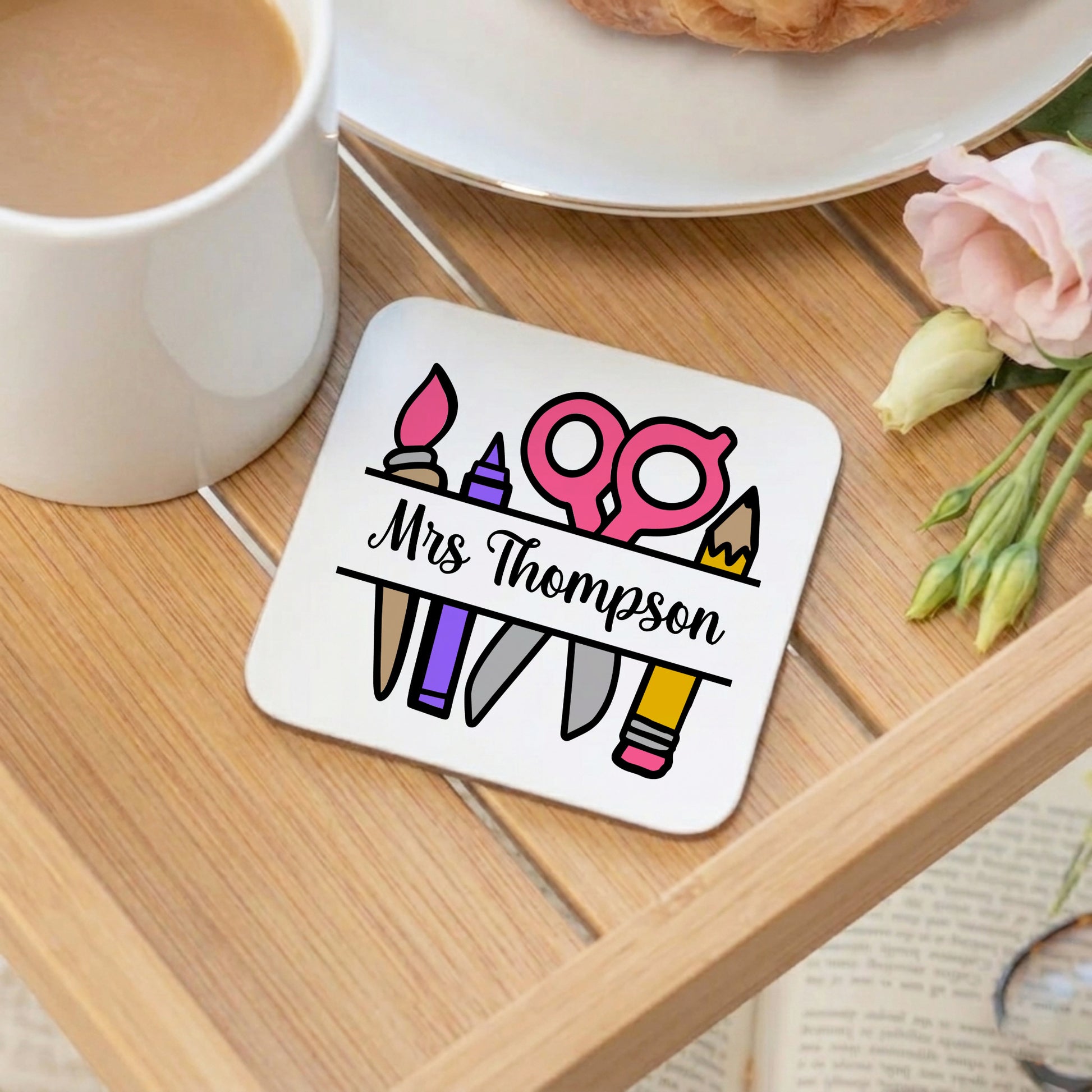 Coaster with personalized design on a wooden table with a cup of coffee and flowers.
