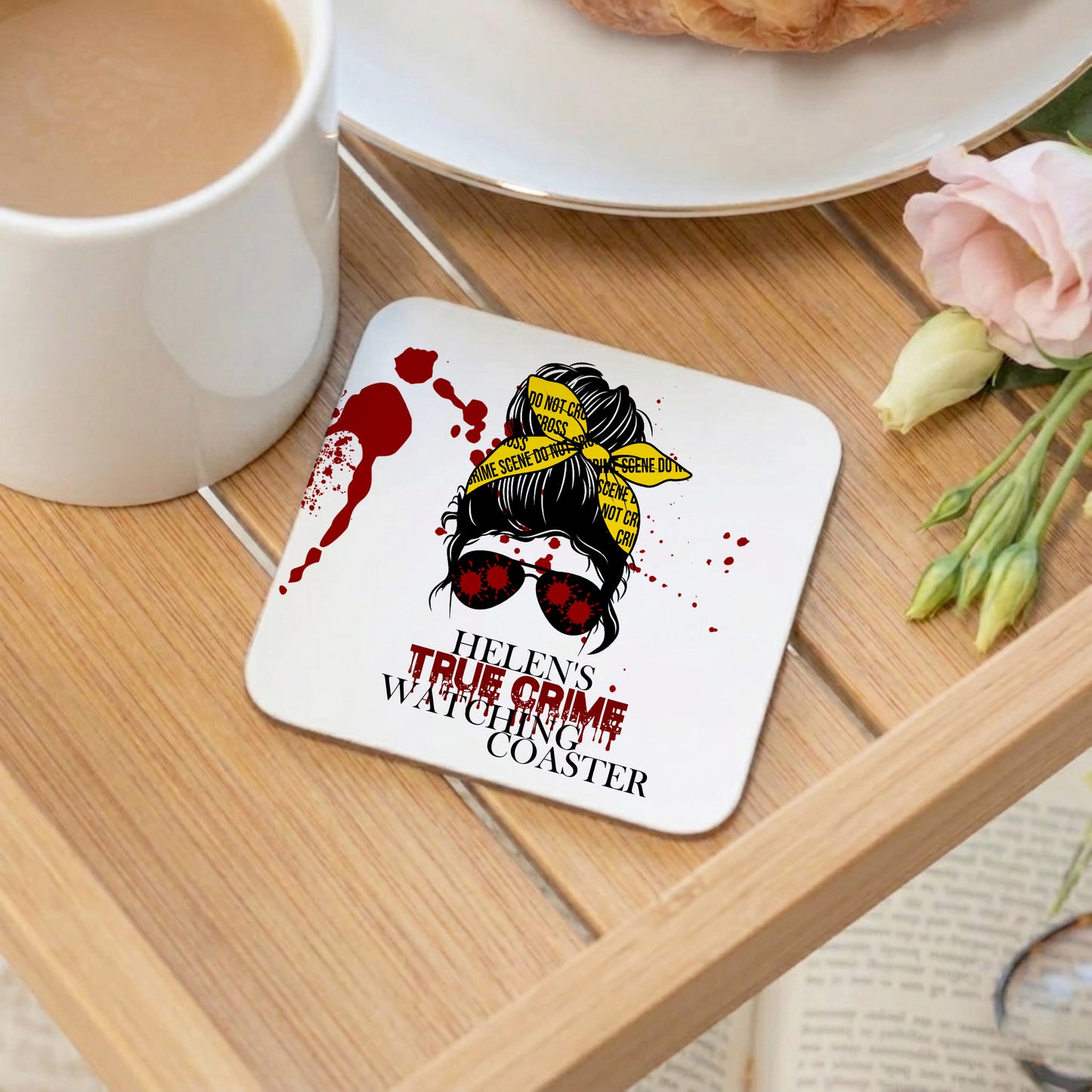 Coaster with a graphic design of a woman with sunglasses and text 'Helen's True Crime Watching Coaster' on a wooden table with a cup of coffee and flowers.