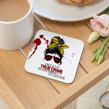 Coaster with a graphic design of a woman with sunglasses and text 'Helen's True Crime Watching Coaster' on a wooden table with a cup of coffee and flowers.