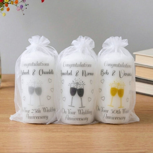 Three wrapped candles in sheer bags with wedding anniversary designs on a wooden surface.