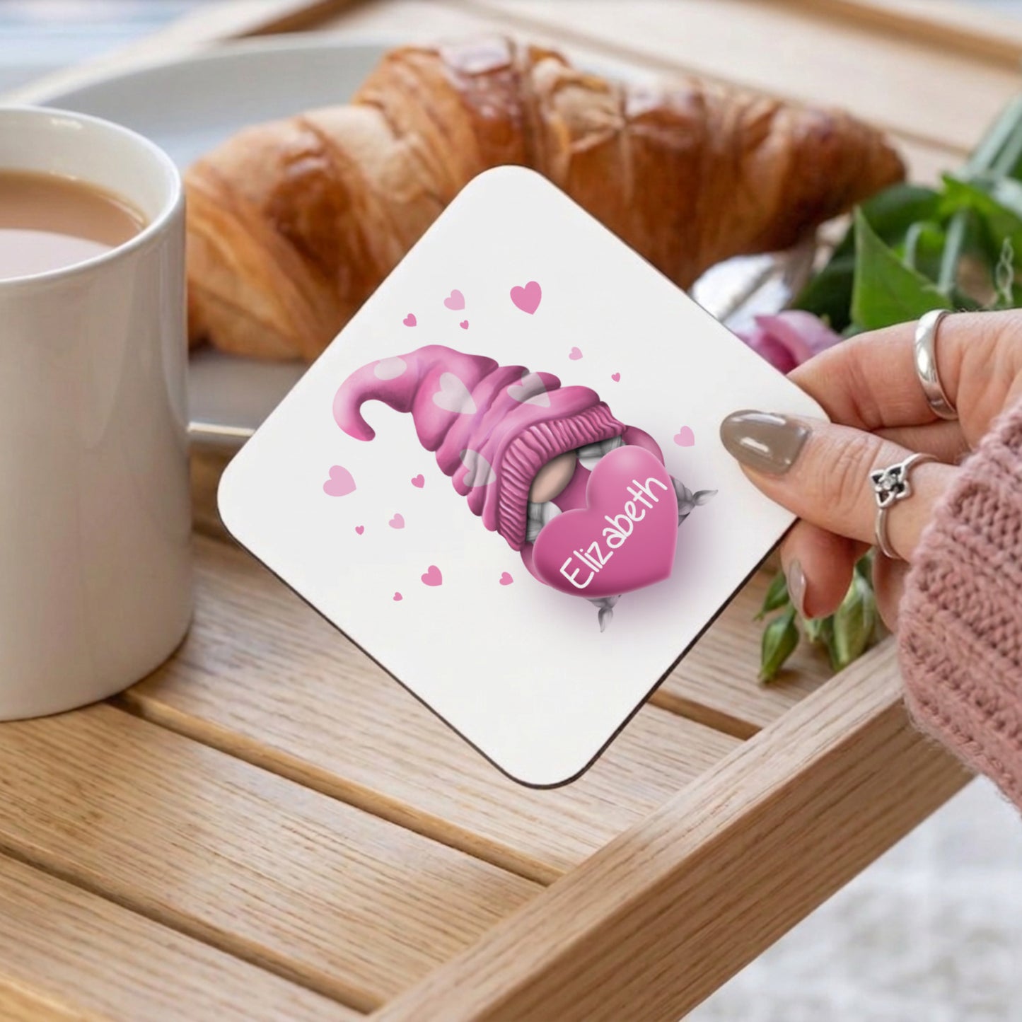 A square coaster with a pink gnome holding a heart with the name "Elizabeth" on it. The gnome wears a pink hat and a pink and white striped sweater. Small pink hearts are scattered around the gnome.
