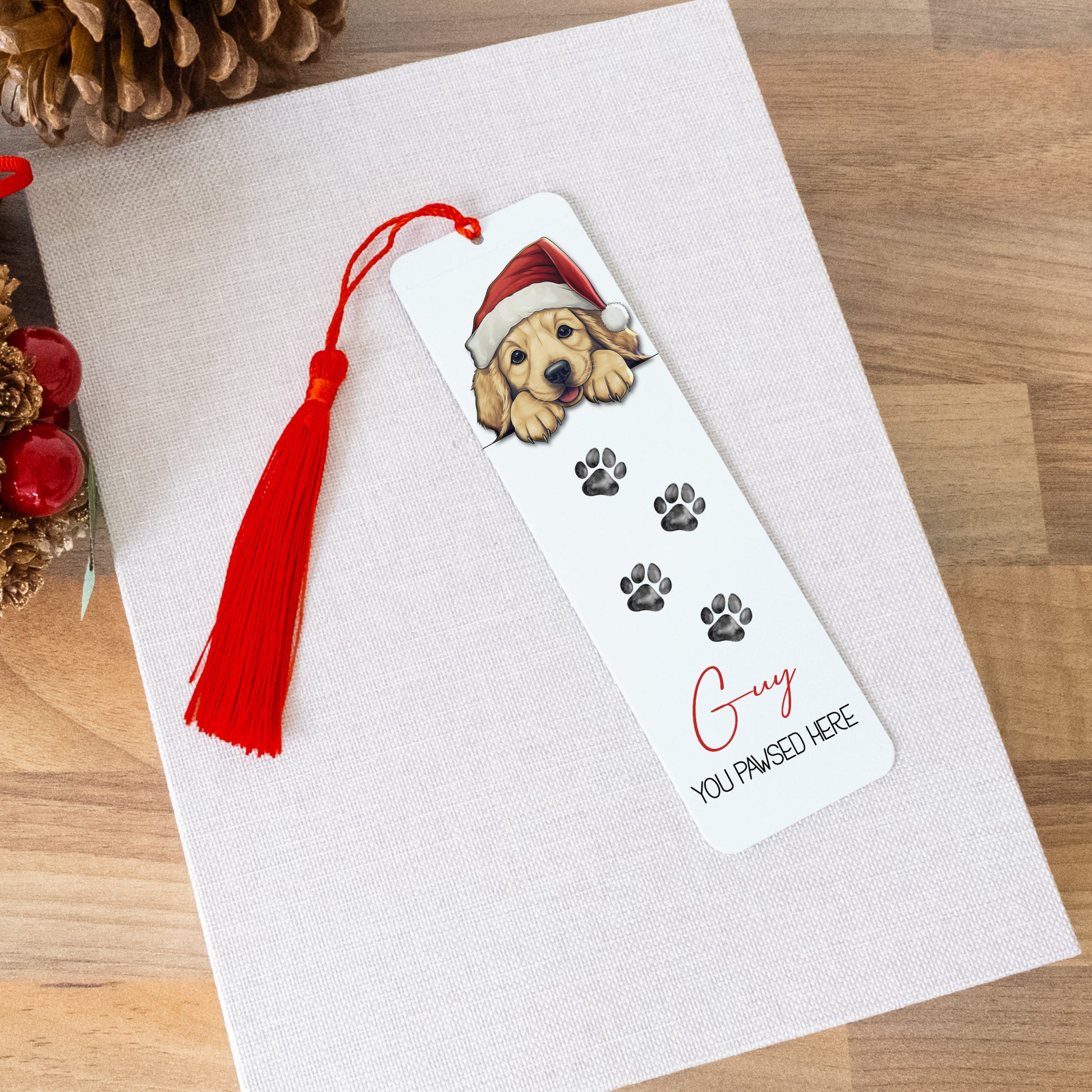 Bookmark with a dog illustration and red tassel on a white card, surrounded by Christmas decorations.