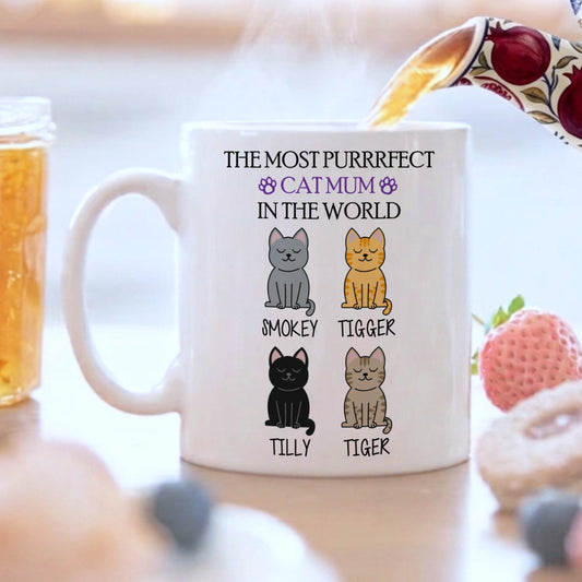Mug with cat illustrations and text on a table with food and tea.