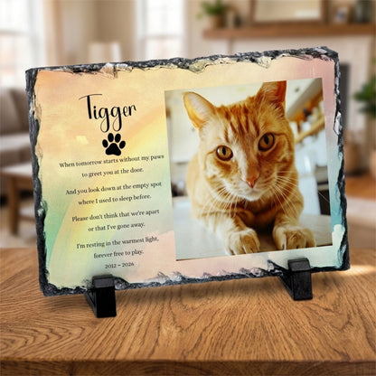 A personalised memorial slate plaque on a black stand, featuring a photo of an orange tabby cat and a poem titled 'Tigger' with a paw print, displayed on a wooden table.