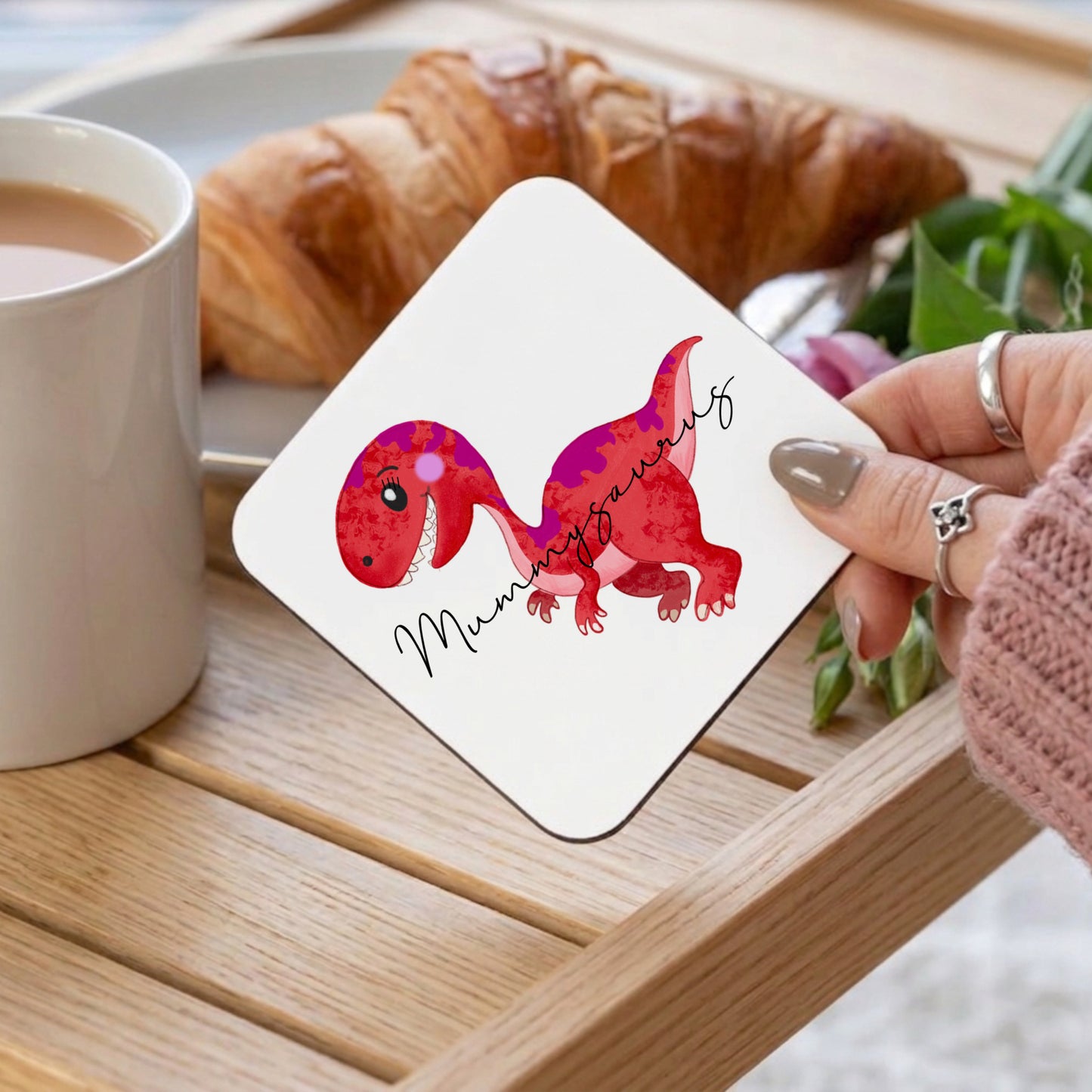 Card with dinosaur illustration held by a hand over a croissant and coffee.