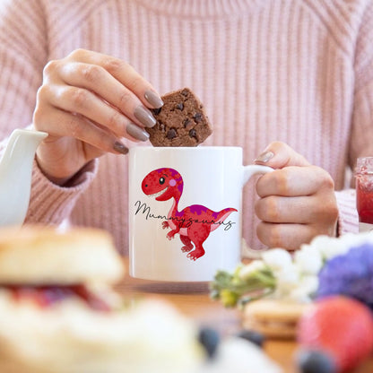 Person holding a mug with a dinosaur design and a cookie, blurred background