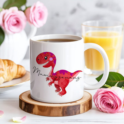 White mug with a red dinosaur design and 'Mummyaurus' text on a wooden coaster, surrounded by pink roses and a glass of orange juice.