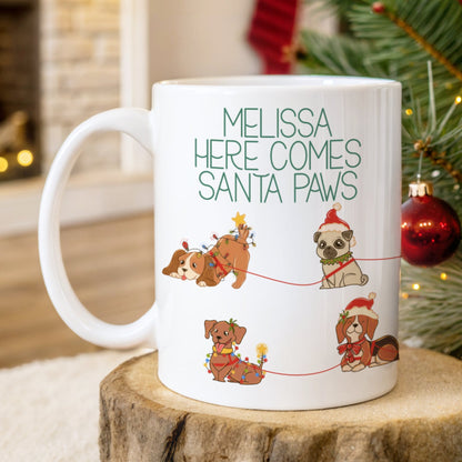 White mug with Christmas-themed design of dogs and text 'Melissa Here Comes Santa Paws' on a wooden surface with a festive background.