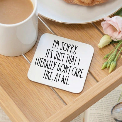 A white square coaster on a breakfast tray with the text "I'm sorry, it's just that I don't care. Like, at all". With a cup of tea, croissant and pink rose 