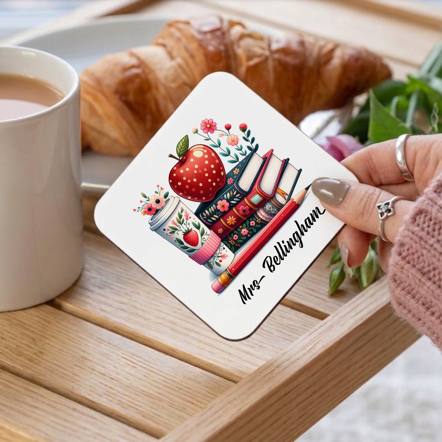 A person holding a personalised teacher coaster with colourful stacked books and red apple design, customised with a teacher's name