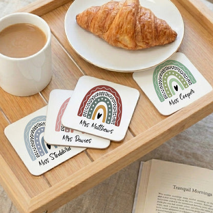Coasters with rainbow designs and names on a wooden tray with coffee and a croissant.