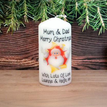 Personalized Christmas candle with Santa Claus design on a wooden surface with greenery in the background.