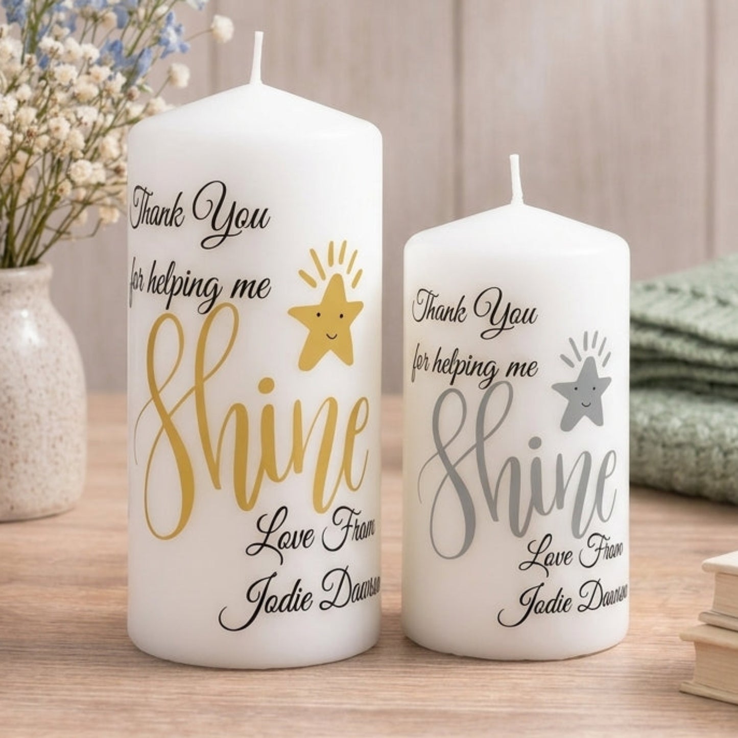 Two white pillar candles with personalised messages printed on them, one smaller and one larger, both with the same design and colour scheme, placed on a red surface.