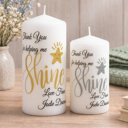 Two white pillar candles with personalised messages printed on them, one smaller and one larger, both with the same design and colour scheme, placed on a red surface.