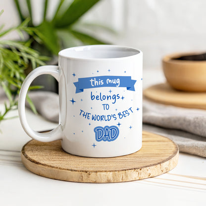 White mug with blue text on a wooden coaster, surrounded by plants and kitchen items.