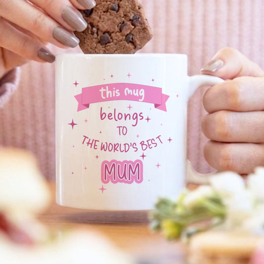 A woman dunking a biscuit into a mug with a design that says this mug belongs to the World's best mum