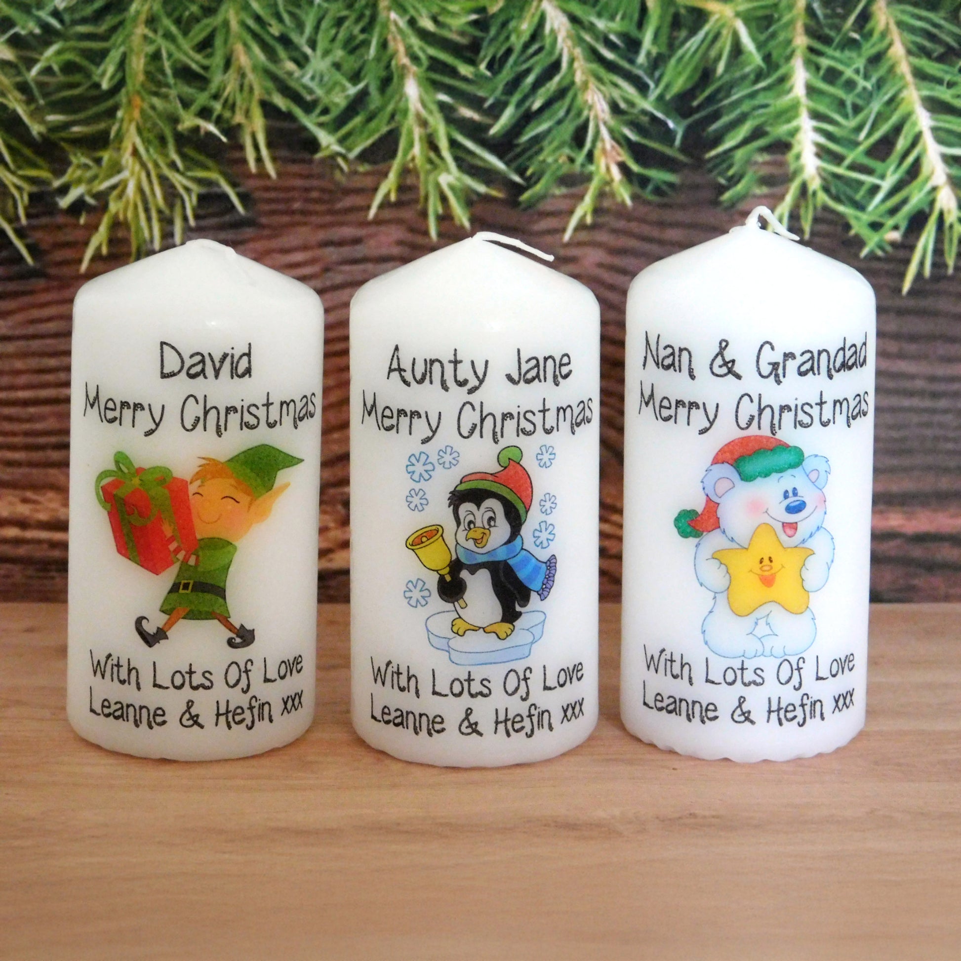 Three personalized Christmas candles with festive designs and text on a wooden surface.