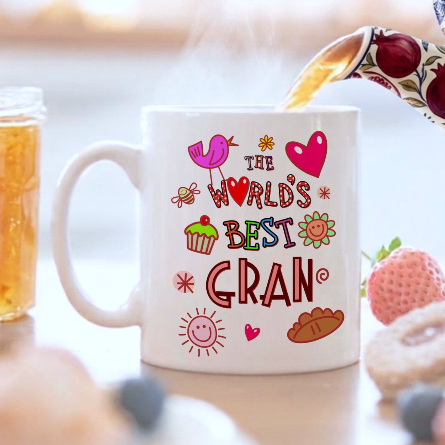 White mug with colorful text 'The World's Best Gran' on a blurred background of food and tea.