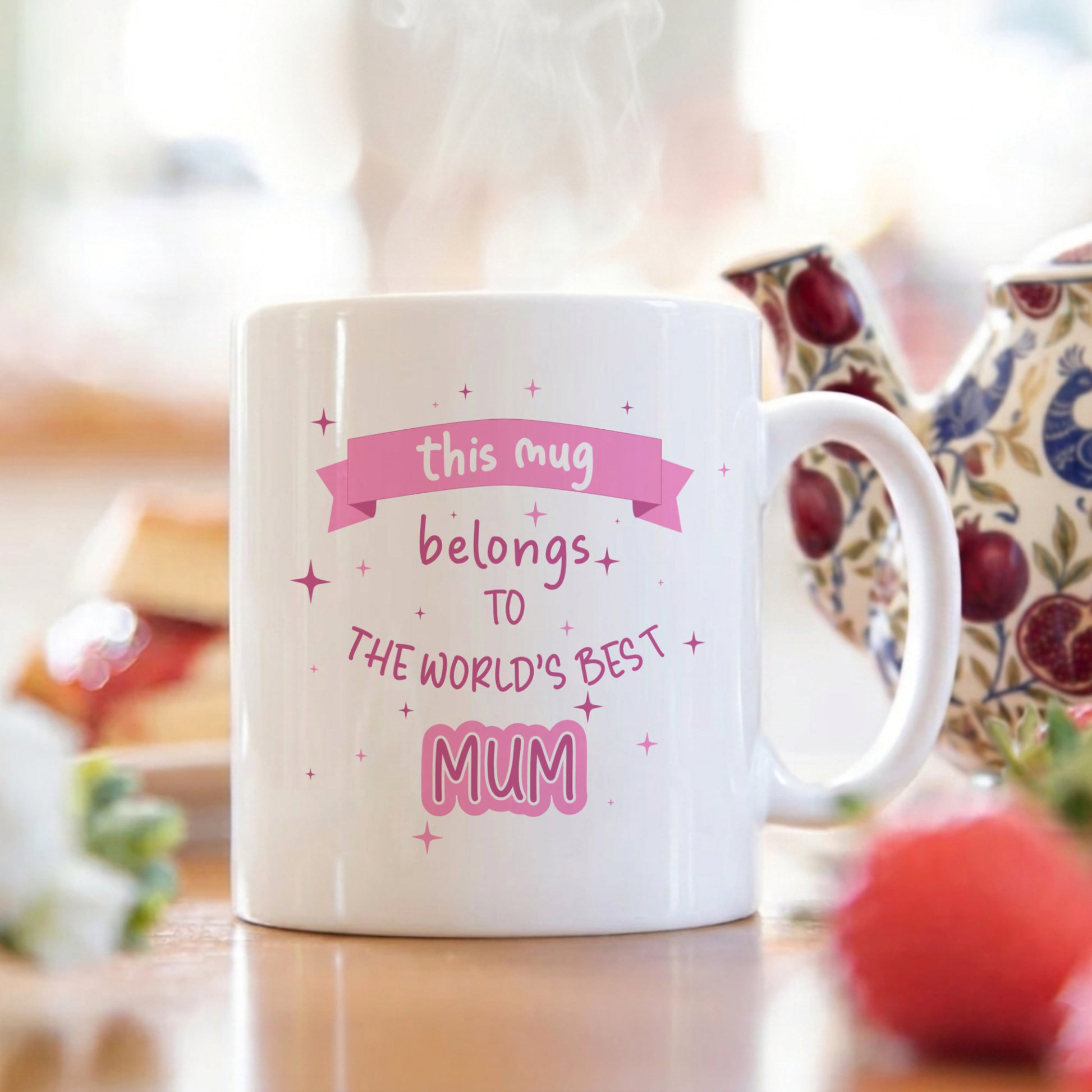 White mug with 'world's best mum' text on a breakfast table with a teapot and blurred background