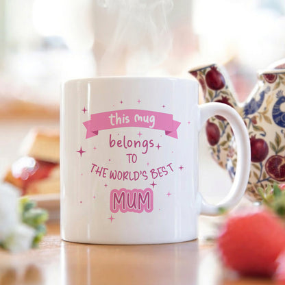 White mug with 'world's best mum' text on a breakfast table with a teapot and blurred background