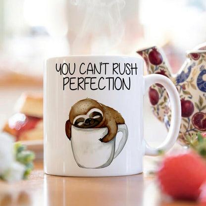 Mug with sloth illustration and 'You can't rush perfection' text on a blurred background