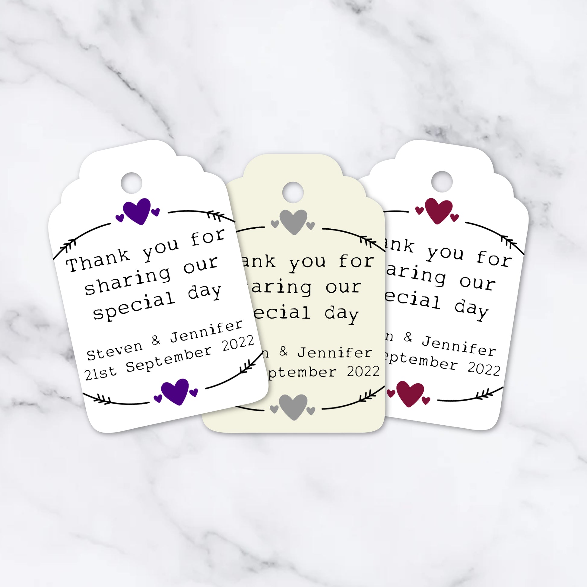 Three personalized heart-shaped wedding tags with white card stock, featuring printed names and a heart design, and a ribbon attachment at the top.